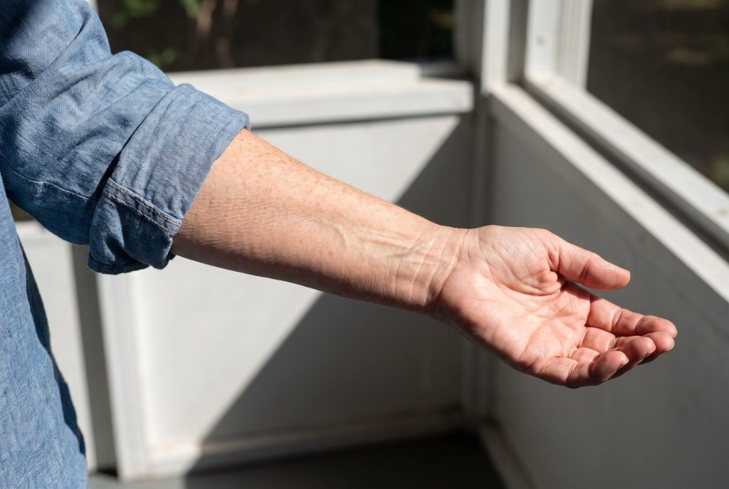 An older woman's forearm turning palm-up in hard sun, the thin skin folding into fine crinkles