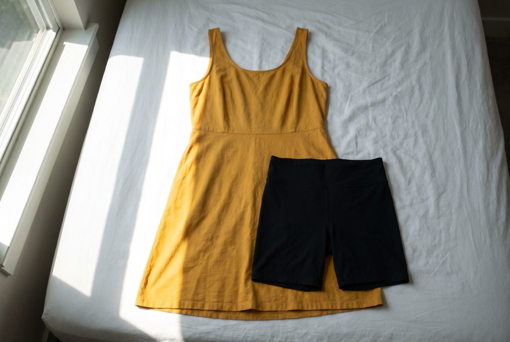 A mustard summer dress and black bike shorts laid out together on a sunlit white bed
