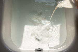 A thin stream of milk pours into a bathtub of clear water, unfurling into silky white wisps