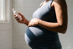 A pregnant woman rests one hand on her belly and reads the back of a plain white lotion bottle